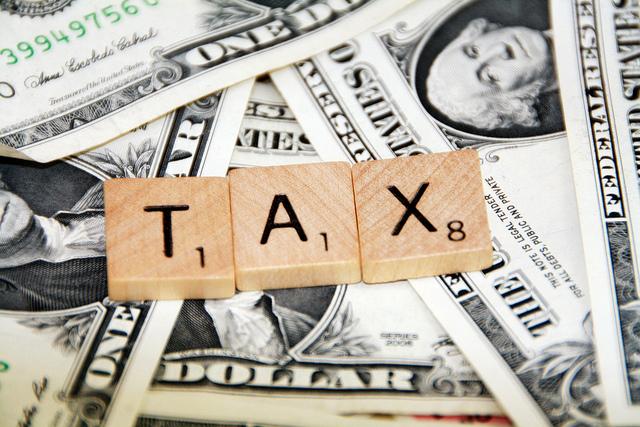 Scrabble tiles spelling out TAX over dollar bills. Significant tax debt can lead to your passport being revoked.
