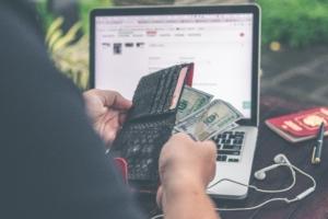 Person holding 100 U.S. dollar bill in front of laptop